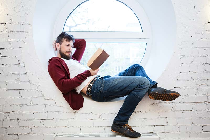 Geschenke für Männer: Ein Mann liest entspannt in einem Fenster ein Buch