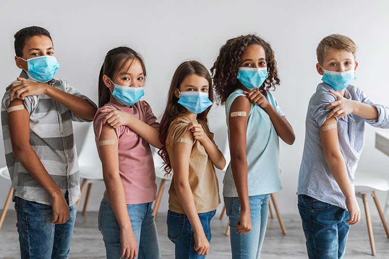 Eine Gruppe von 5 Kinder zeigen mit Maske ihr Pflaster vom impfen gegen Corona