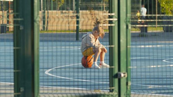 Ein Junge sitzt traurig auf einem Basketball. Wartet er auf das Ergebnis eines Familiengerichtverfahrens?
