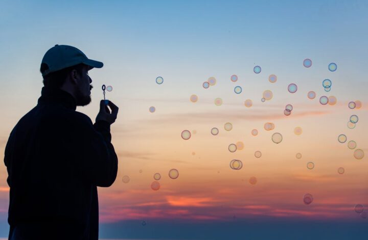 Ein Mann mit Cappi pustet Seifenblasen in den Sonnenuntergang. Das Bild symbolisiert den Vatertag