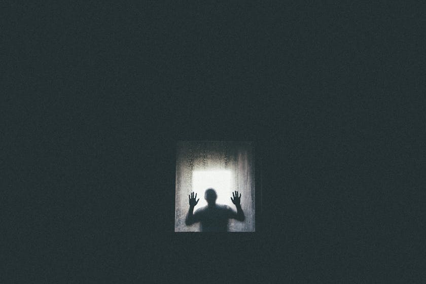 Eine Person hinter einer feuchten Glasscheibe legt die Hände ans Fenster. Als Schattenbild symbolisiert es psychische Erkrankungen